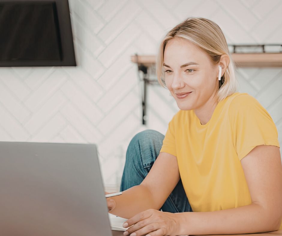 A smiling first-time fiction writer in a yellow shirt working on her novel manuscript on a laptop.