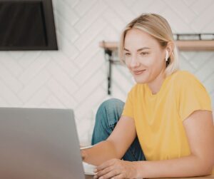 A smiling first-time fiction writer in a yellow shirt working on her novel manuscript on a laptop.
